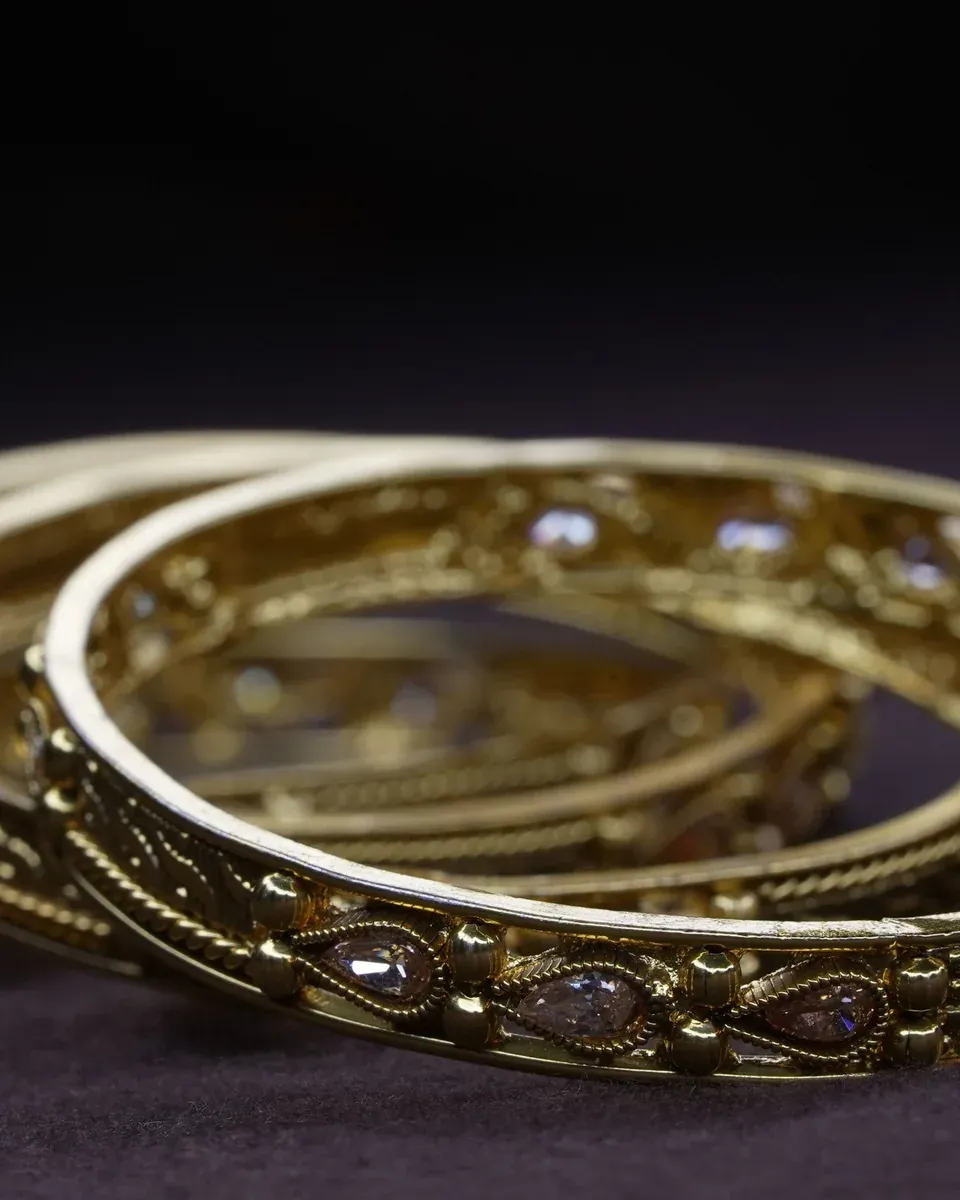 Verzierte Armreifen aus Gold mit kleinen Steinen auf dunklem Samt
