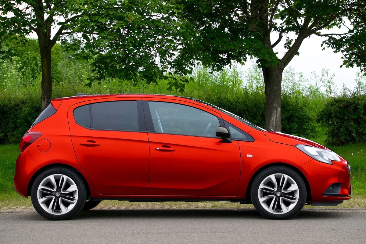 Roter Opel Corsa von der Seite vor Bäumen