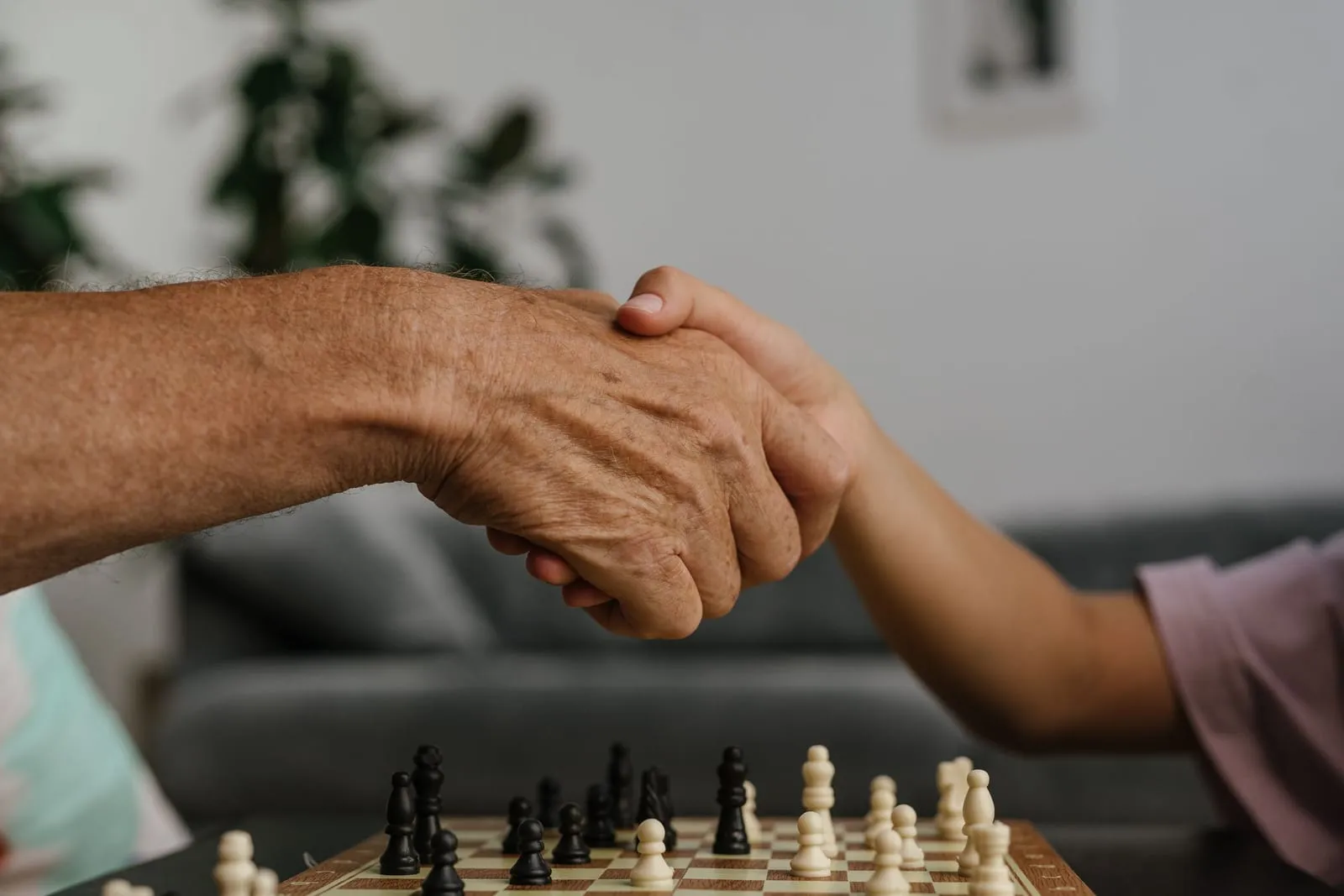Eine junge und eine ältere Hand reichen sich über einem Schachbrett die Hand