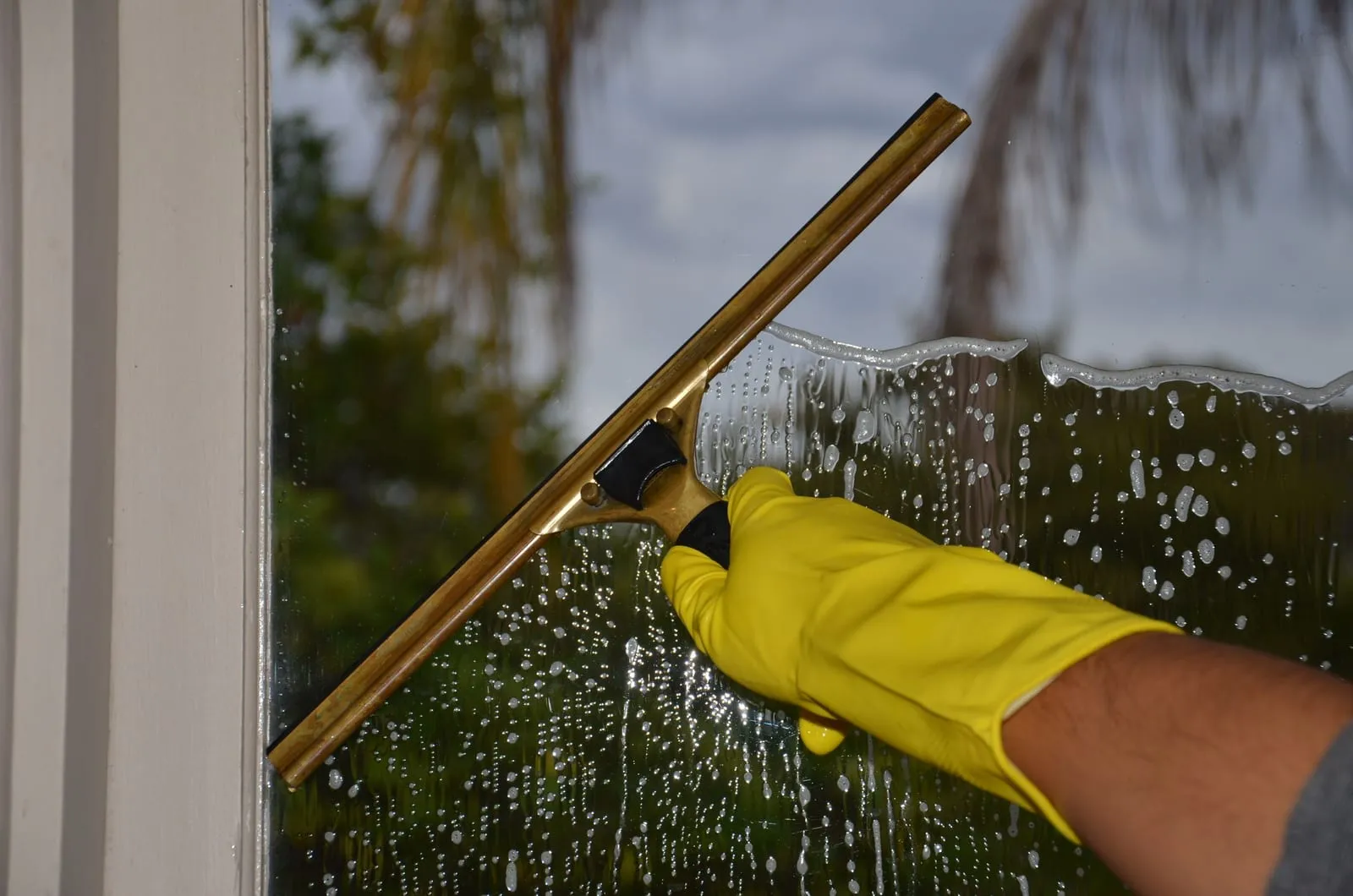 Hand im gelben Handschuh zieht einen Fensterwischer über eine eingeseifte Scheibe
