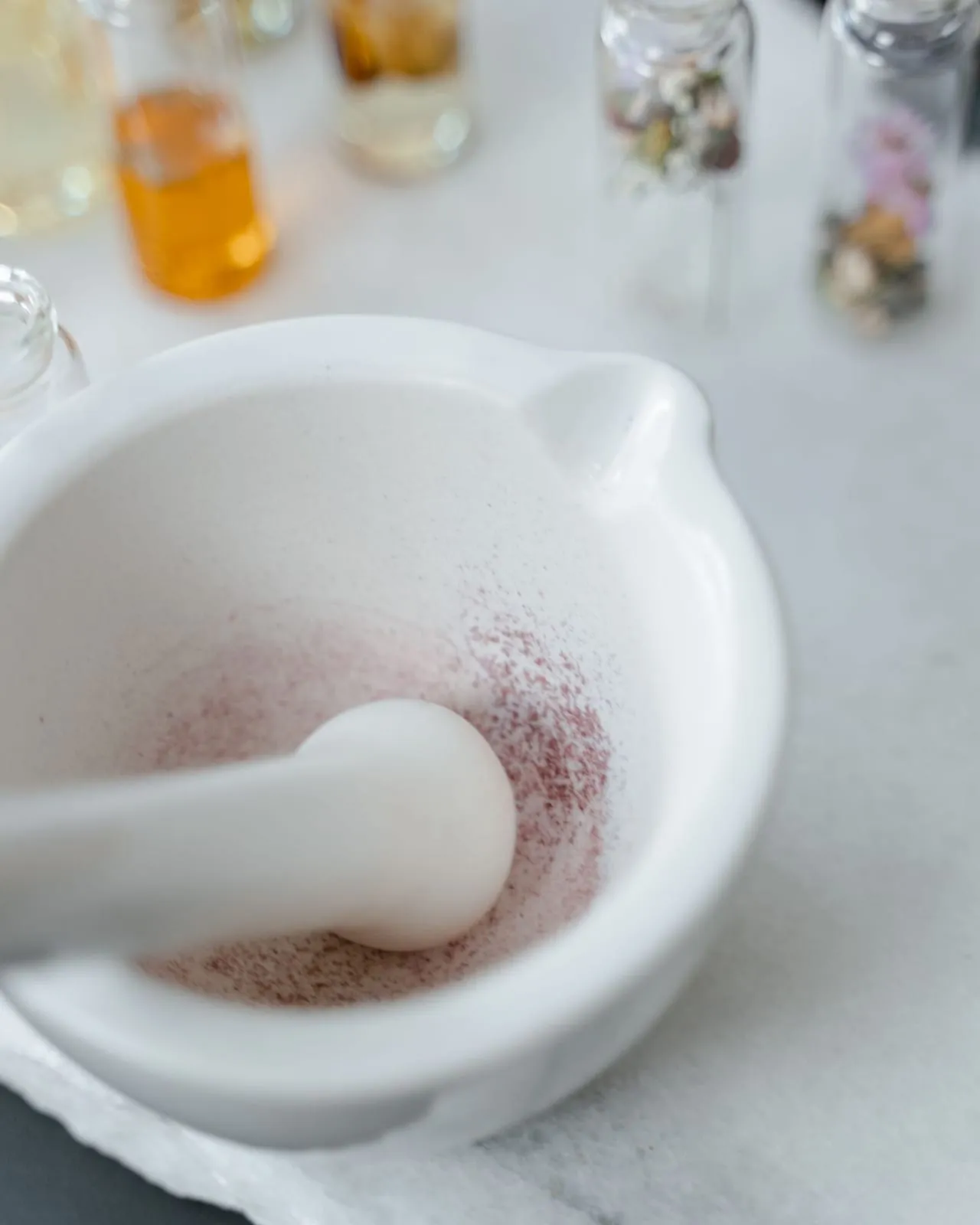 Mörser und Pistill aus weißem Marmor, dahinter kleine Glasflaschen