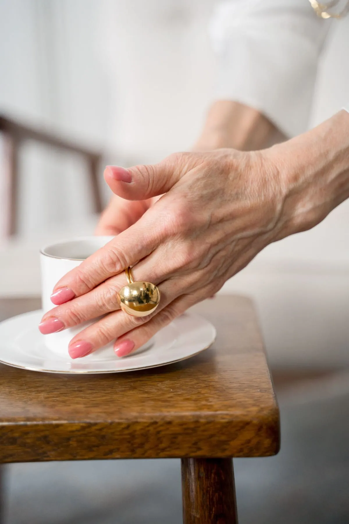 Eine ältere Hand mit goldenem Ring liegt auf einer Teetasse