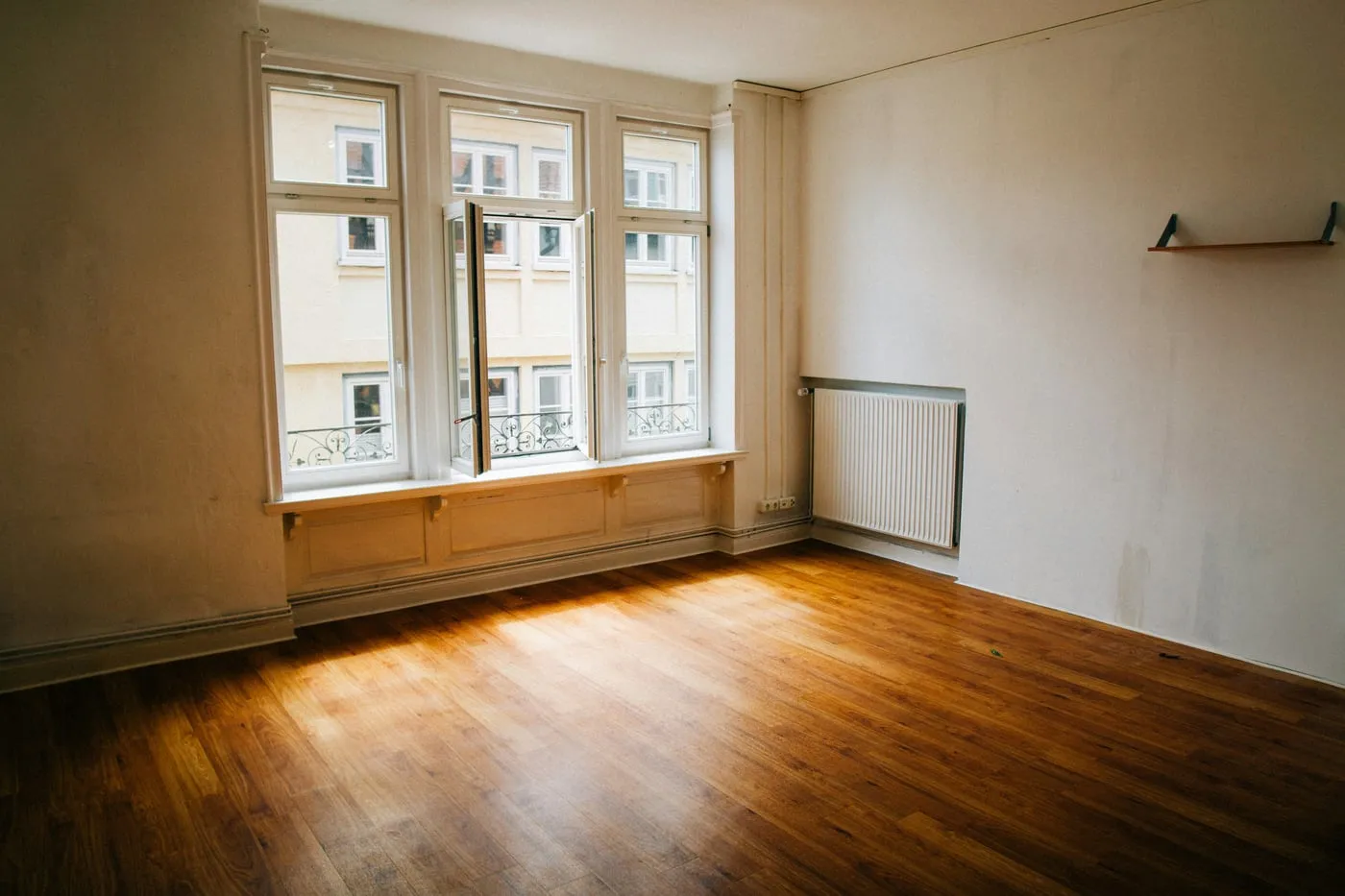 Leere Altbauwohnung mit hohen Sprossenfenstern und Holzboden in der Abendsonne