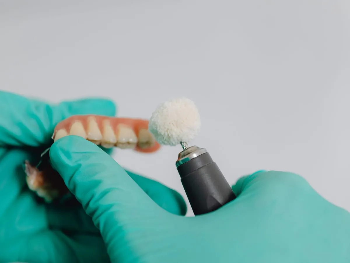 Hände in Handschuhen polieren eine Zahnprothese